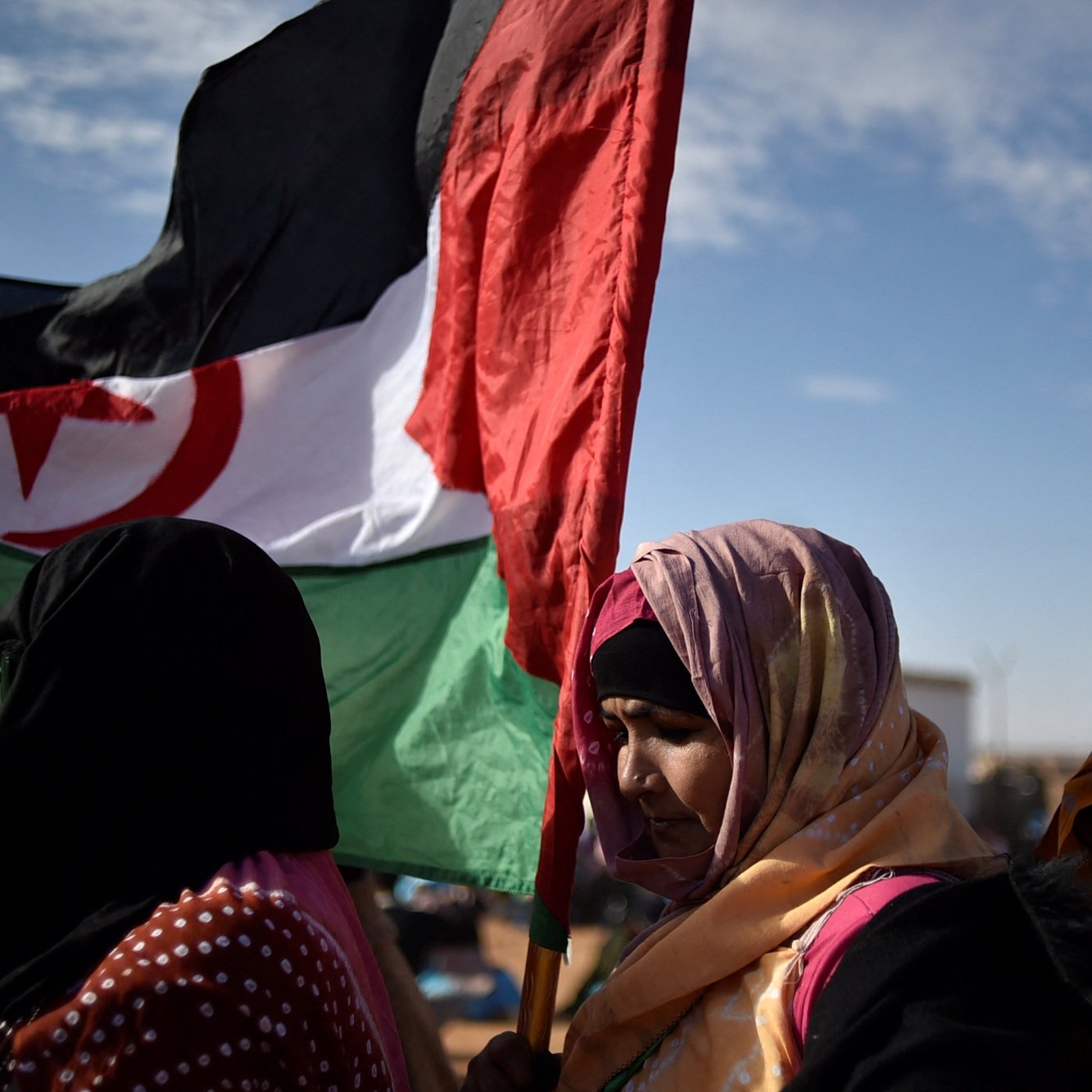 Des femmes portant une écharpe colorée et une grande bannière. Ciel dégagé en arrière-plan.