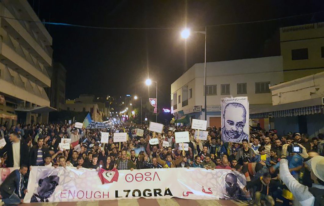 الصورة تظهر حشودًا كبيرة من الناس في تجمع أو مظاهرة في شارع ليلي. يرفع المتظاهرون لافتات، بعضها يحمل شعارات تعبر عن مطالب أو قضايا معينة. في الخلفية، يمكن رؤية مباني متجاورة وأضواء الشارع. تُظهر الصورة حماسًا وتفاعلًا اجتماعيًا بين المشاركين، مما يدل على أهمية الحدث الذي يجمعهم.