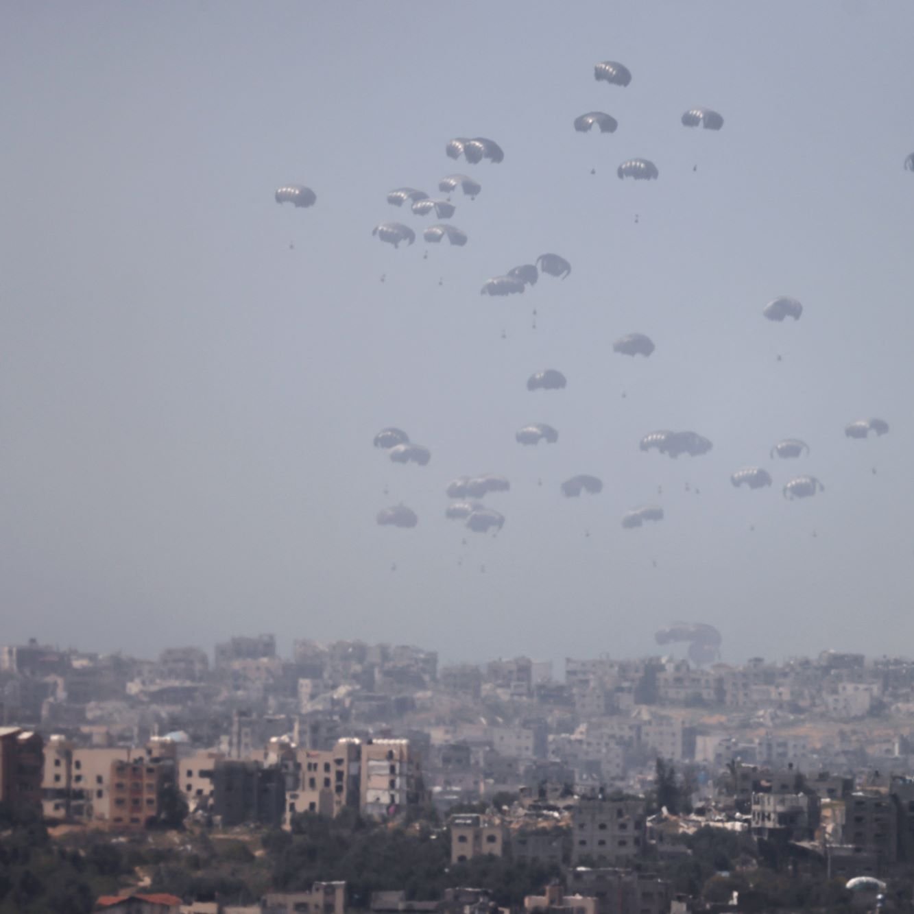 در این تصویر، چندین چتر نجات در آسمان به طور هم‌زمان دیده می‌شوند که به آرامی در حال سقوط هستند. زمینه تصویر شهری است که شامل ساختمان‌ها و محله‌های مختلف است. آسمان ابری و کمی تاریک به نظر می‌رسد و این باعث می‌شود فضای تصویر حالتی جدی و نگران‌کننده داشته باشد. تصویر به خوبی نمایانگر یک وضعیت نظامی یا اضطراری است.