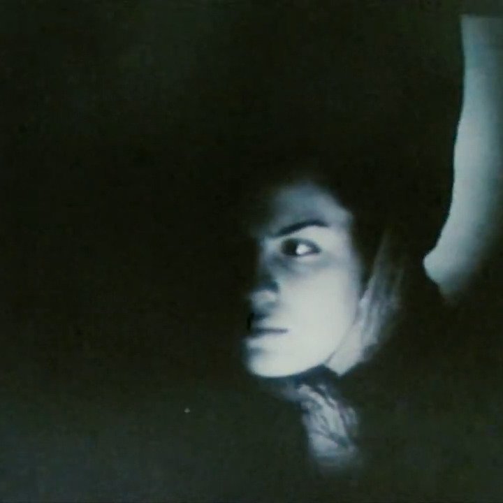L'image présente un contraste marquant entre ombre et lumière, mettant en avant le visage d'une personne. Son expression semble intrigante, avec un regard perçant qui capte l'attention. On distingue également un bras, suggérant une posture dynamique. L'ambiance générale est mystérieuse et un peu sombre, ce qui peut susciter diverses interprétations émotionnelles.