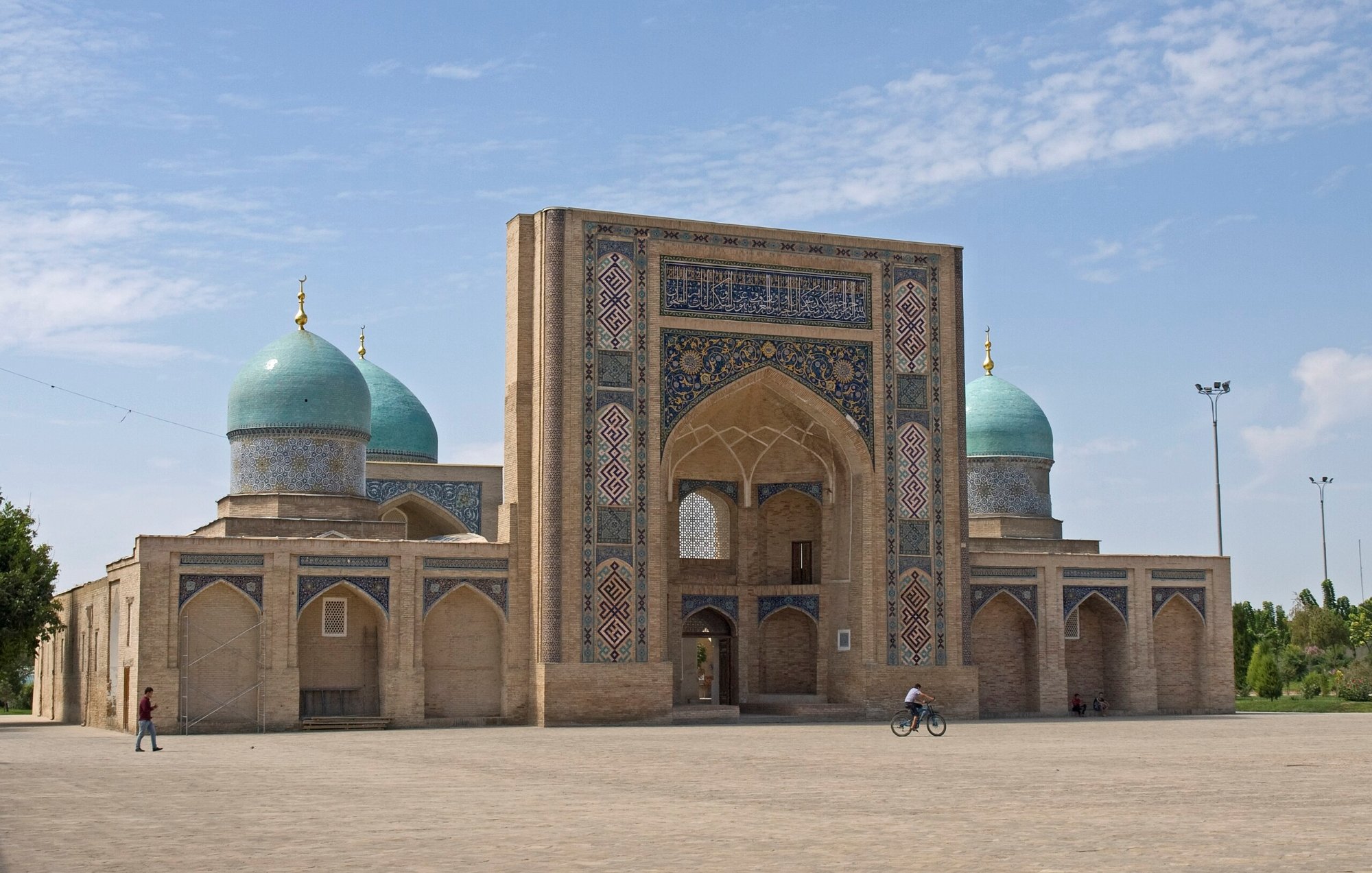 تظهر الصورة معمارًا تاريخيًا بأقواس وقباب زرقاء في سماء صافية. جو مريح.