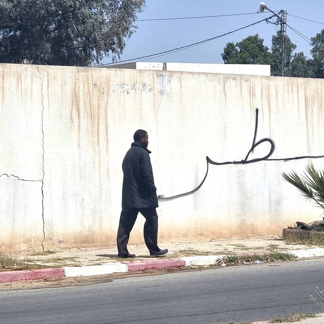 Un homme marche le long d'un mur avec une grande inscription en arabe.
