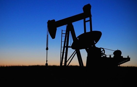 L'image montre un pompage de pétrole silhouetté contre un ciel au crépuscule. On peut voir la structure du pompage avec ses bras articulés, ainsi qu'une échelle menant à la plateforme. Le fond présente des dégradés de bleu et d'orange, indiquant le moment de la journée où le soleil se couche. L'ensemble dégage une ambiance tranquille tout en évoquant l'industrie pétrolière.