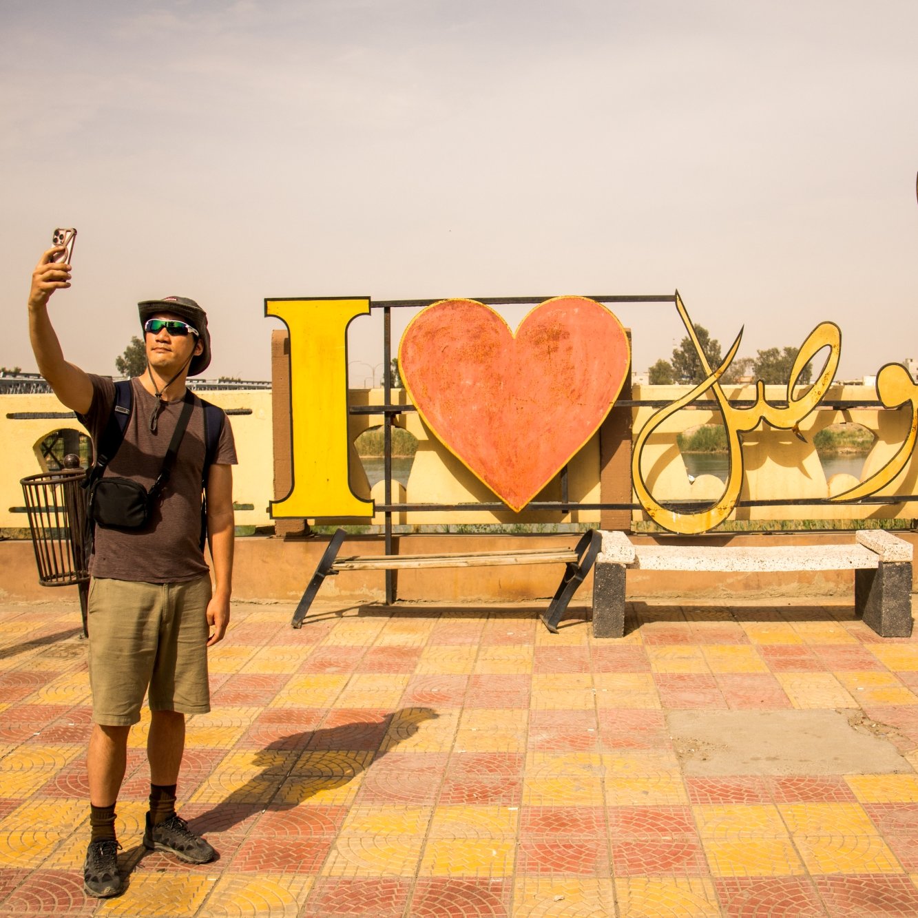 Un uomo fa un selfie davanti a un grande cartello colorato con "I ❤️" e fiori.