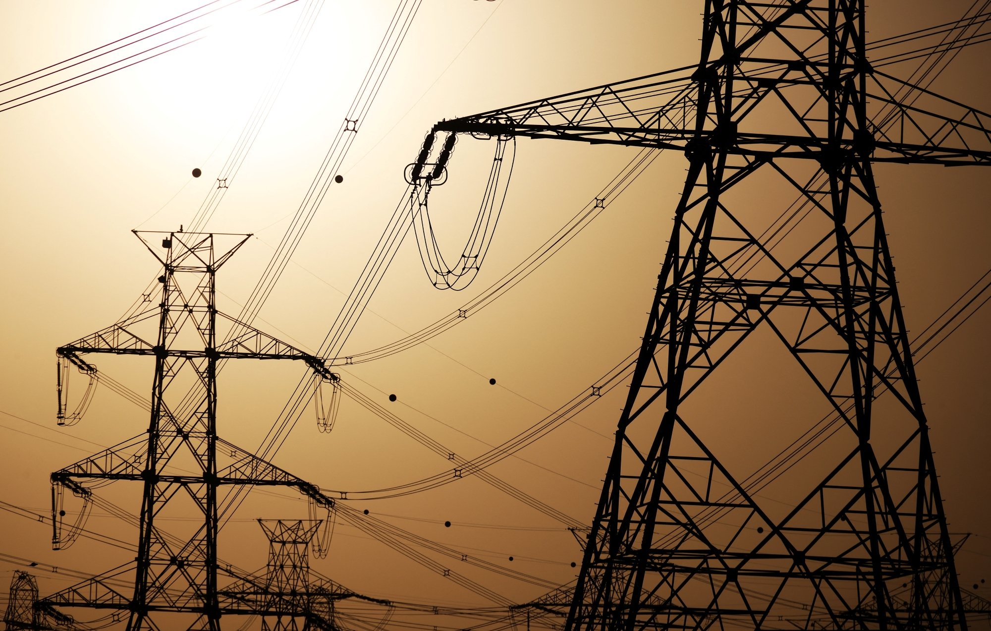 Silhouettes de pylônes électriques contre un ciel orangé.