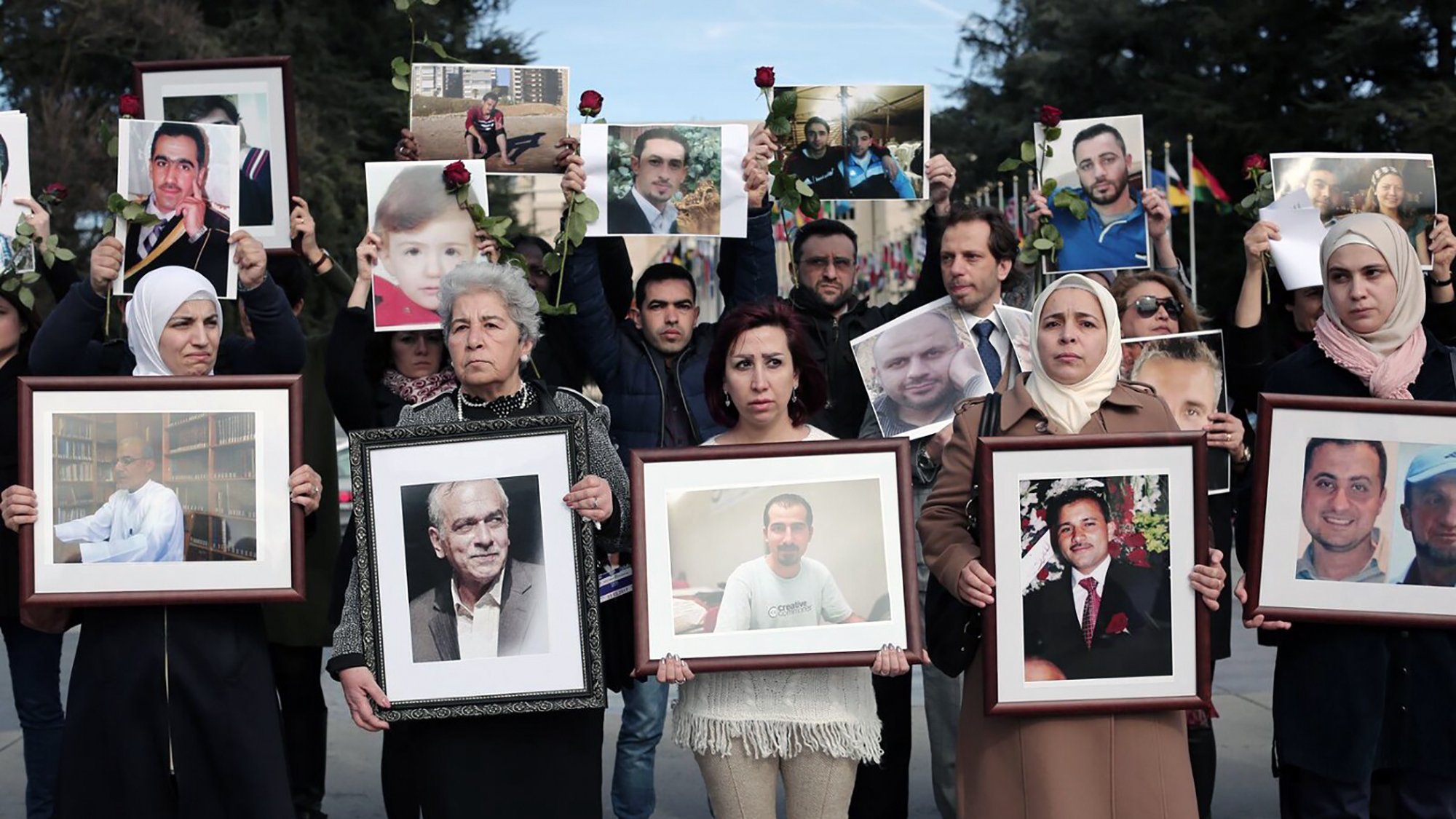 در این تصویر، گروهی از مردم در حال برگزاری تجمعی هستند. آن‌ها عکس‌هایی از افراد مختلف را در دست دارند که به نظر می‌رسد عزیزانشان باشند. در این تجمع، تعدادی زن و مرد حضور دارند، برخی از آن‌ها چهره‌هایشان را با گل‌هایی تزئین کرده‌اند. احساساتی نظیر ناراحتی و یادآوری در چهره‌های حاضرین مشهود است. این تصاویر ممکن است نشان‌دهنده یادمان یا اعتراضی برای یادآوری افرادی باشد که از دست رفته‌اند.