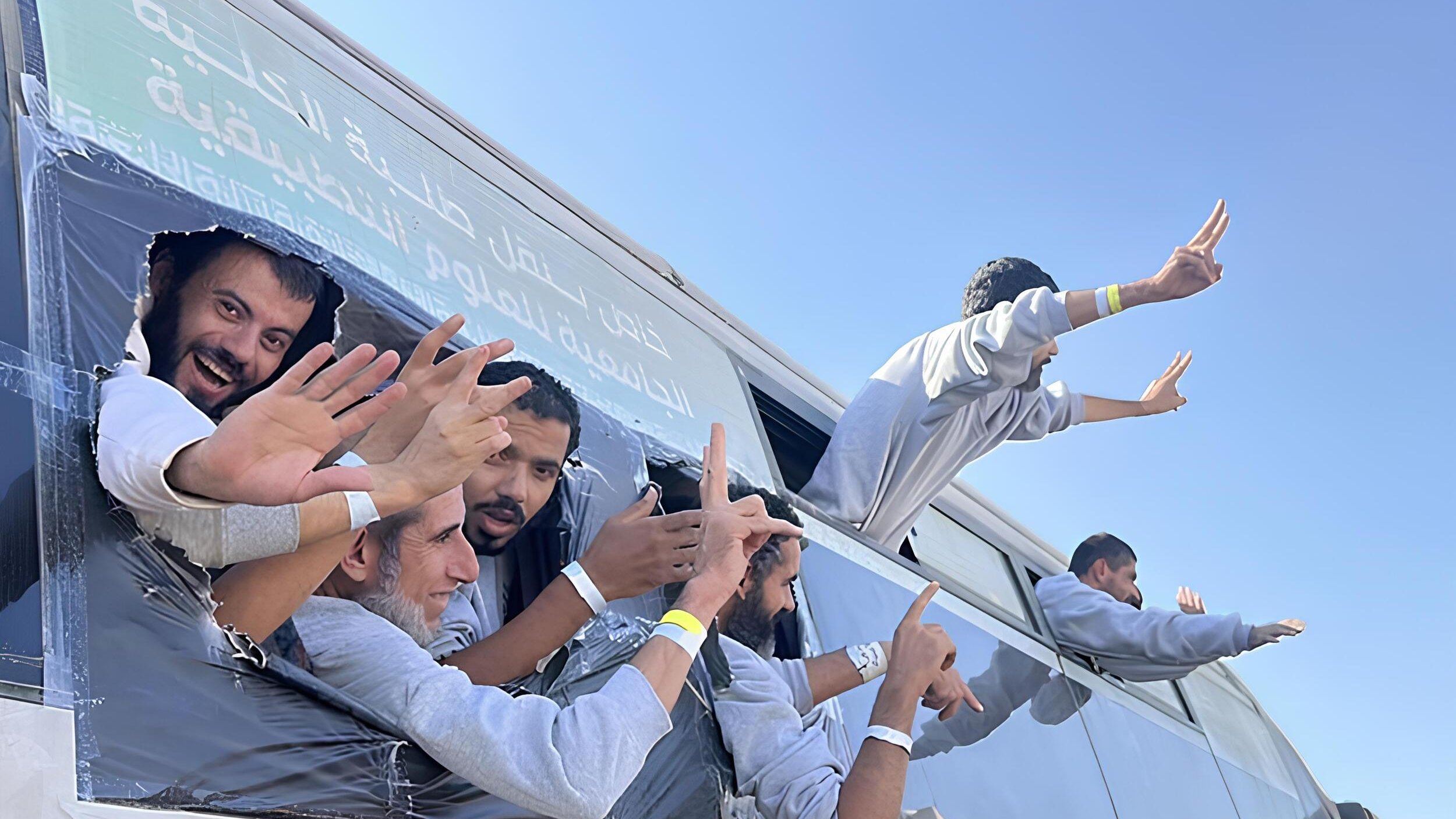 Gruppo di persone sorridenti sporge da un bus con le mani alzate, in un'atmosfera festosa.