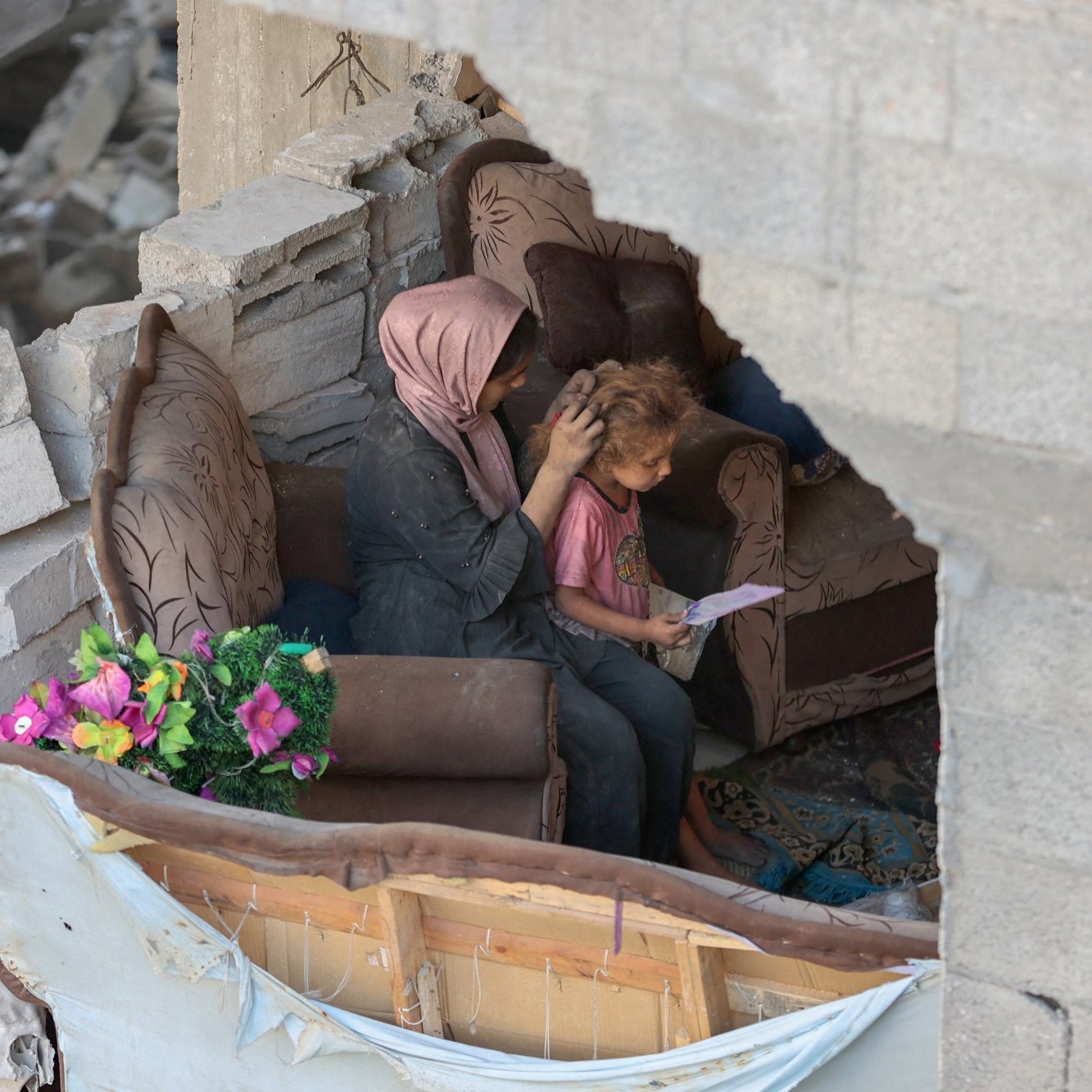 Due persone sedute su un divano in un ambiente distrutto, circondate da macerie.