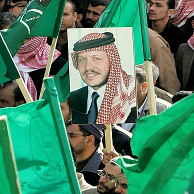 L'image montre une foule rassemblée, tenant des drapeaux verts. Au centre, il y a un portrait d'un homme, probablement une figure importante, qui est mis en avant parmi les drapeaux. L'atmosphère semble être celle d'une manifestation ou d'un rassemblement politique, avec des participants engagés et un message de soutien collectif.