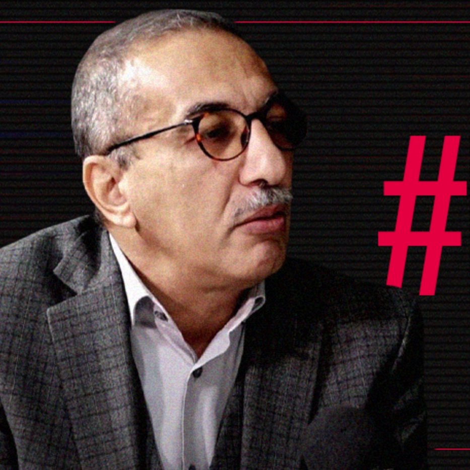 L'image montre un homme portant des lunettes et un costume à carreaux. Il semble participer à une interview ou à un débat, étant tourné vers un interlocuteur. À côté de lui, le texte en gras indique "#Free Ihsane ElKadi", suggérant qu'il est lié à une campagne de sensibilisation ou de soutien pour cette personne. L'arrière-plan présente un design graphique sobre, probablement pour mettre en avant le message.