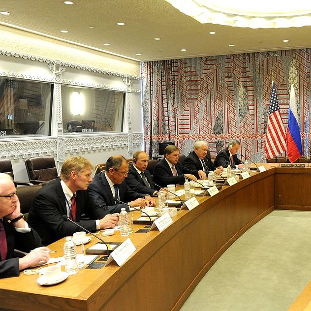 تظهر في الصورة مجموعة من المسؤولين في قاعة اجتماعات. الجانبان يمثلان الولايات المتحدة وروسيا، مع وجود علمي كلا البلدين على الطاولة. يبدو أن الاجتماع يتناول قضايا دبلوماسية أو سياسية هامة. الطاولة طويلة، وهناك عدد من الكراسي المحيطة بها، حيث يجلس المشاركون يتبادلون النقاشات. تظهر ملامح الجدية والتركيز على وجوههم، مما يدل على أهمية الحوار الجاري. الديكور الخلفي للمكان يتضمن تصاميم حديثة.