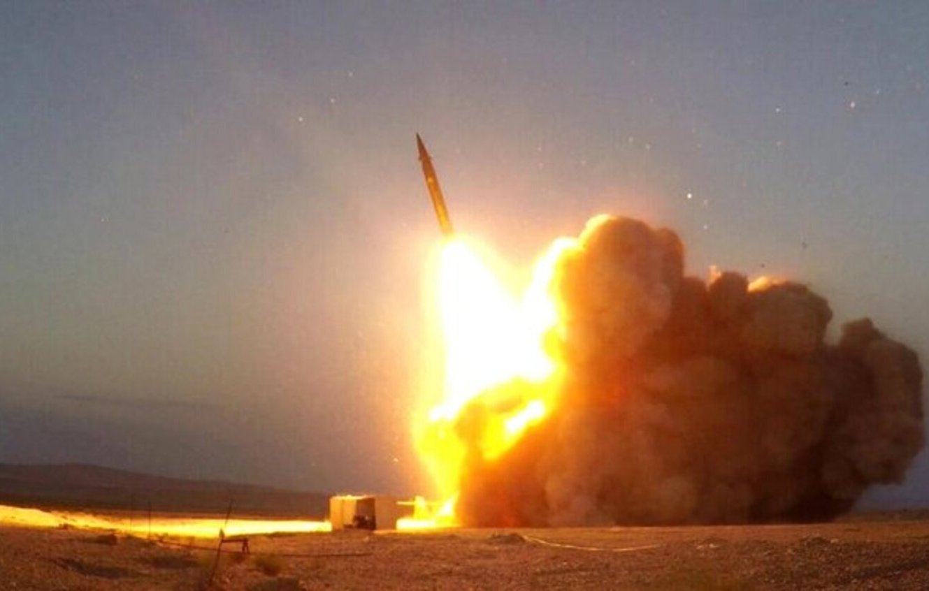 L'immagine mostra un razzo lanciato da un sistema di lancio mobile. Si può notare un intenso getto di fiamme e fumi all'uscita del razzo, accompagnato da una nube di polvere sollevata dal terreno. Il cielo è visibile sullo sfondo, indicando un momento di sera o al crepuscolo, con tonalità che suggeriscono l'imminente oscurità. La scena trasmette una forte impressione di potenza e dinamismo.