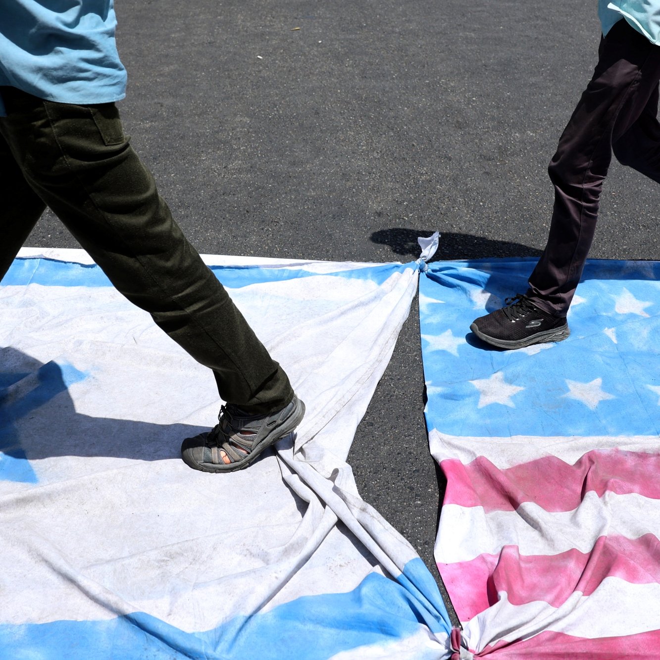 Deux personnes marchent sur des drapeaux américains et cubains étalés au sol.