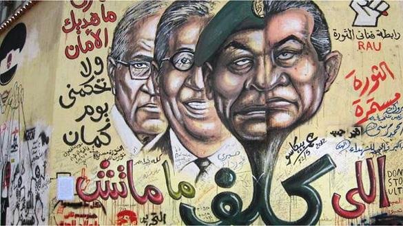 L'image représente une fresque murale avec des portraits de figures politiques, accompagnée de textes en arabe et d'autres éléments graphiques. Les visages semblent se faire face de manière marquante, probablement pour symboliser des conflits ou des idées politiques. Les inscriptions en arabe pourraient évoquer des slogans ou des messages liés à la politique ou à la société. L'utilisation de couleurs vives et de styles artistiques renforce l'impact visuel de cette œuvre.