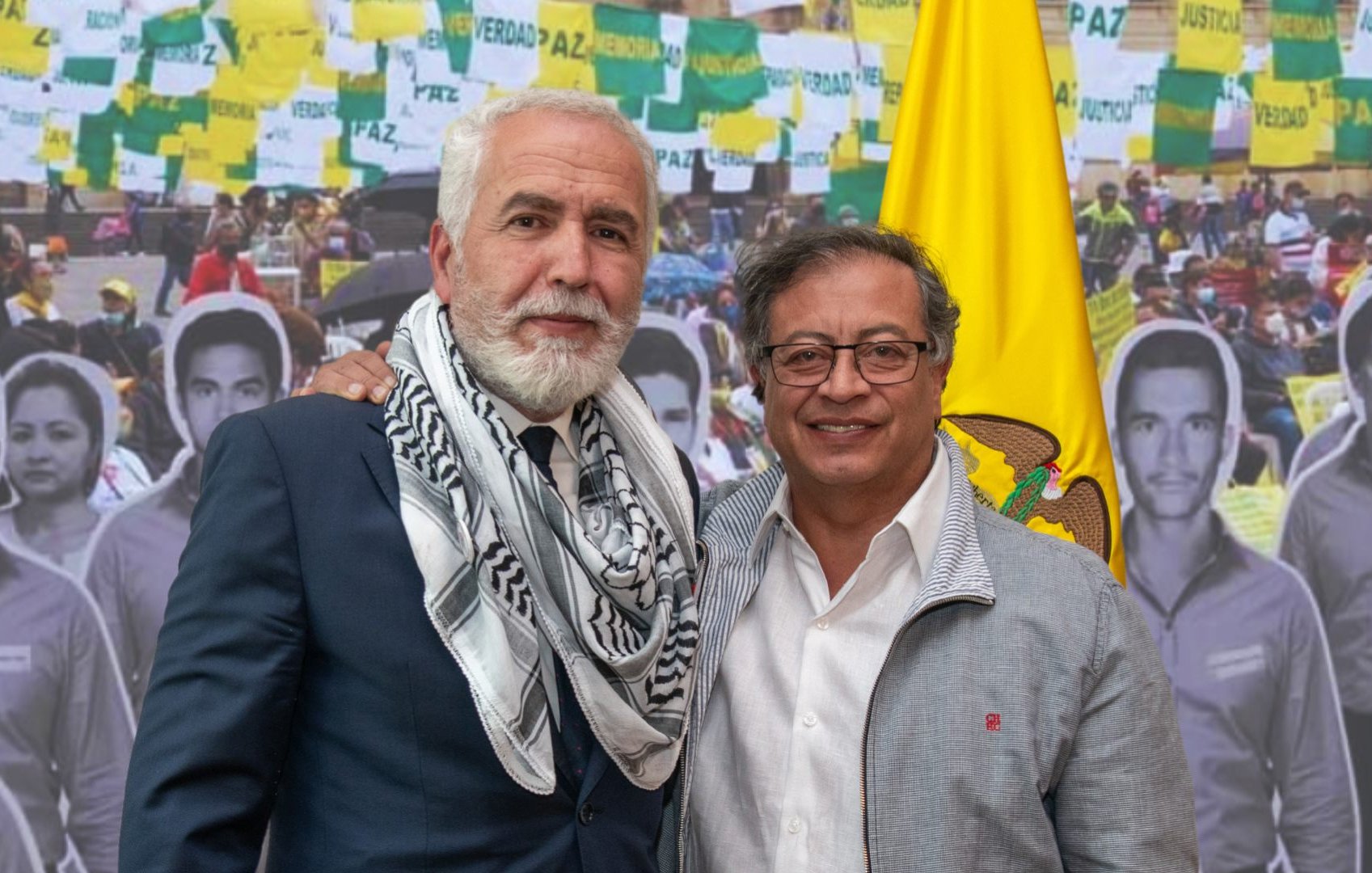 Je ne peux pas identifier les personnes dans l'image. Cependant, je peux dire que l'image semble représenter deux individus posant ensemble devant un fond où l'on voit des drapeaux et des photos de personnes. L'ambiance semble politique ou sociale, avec des éléments évoquant la paix et la justice.