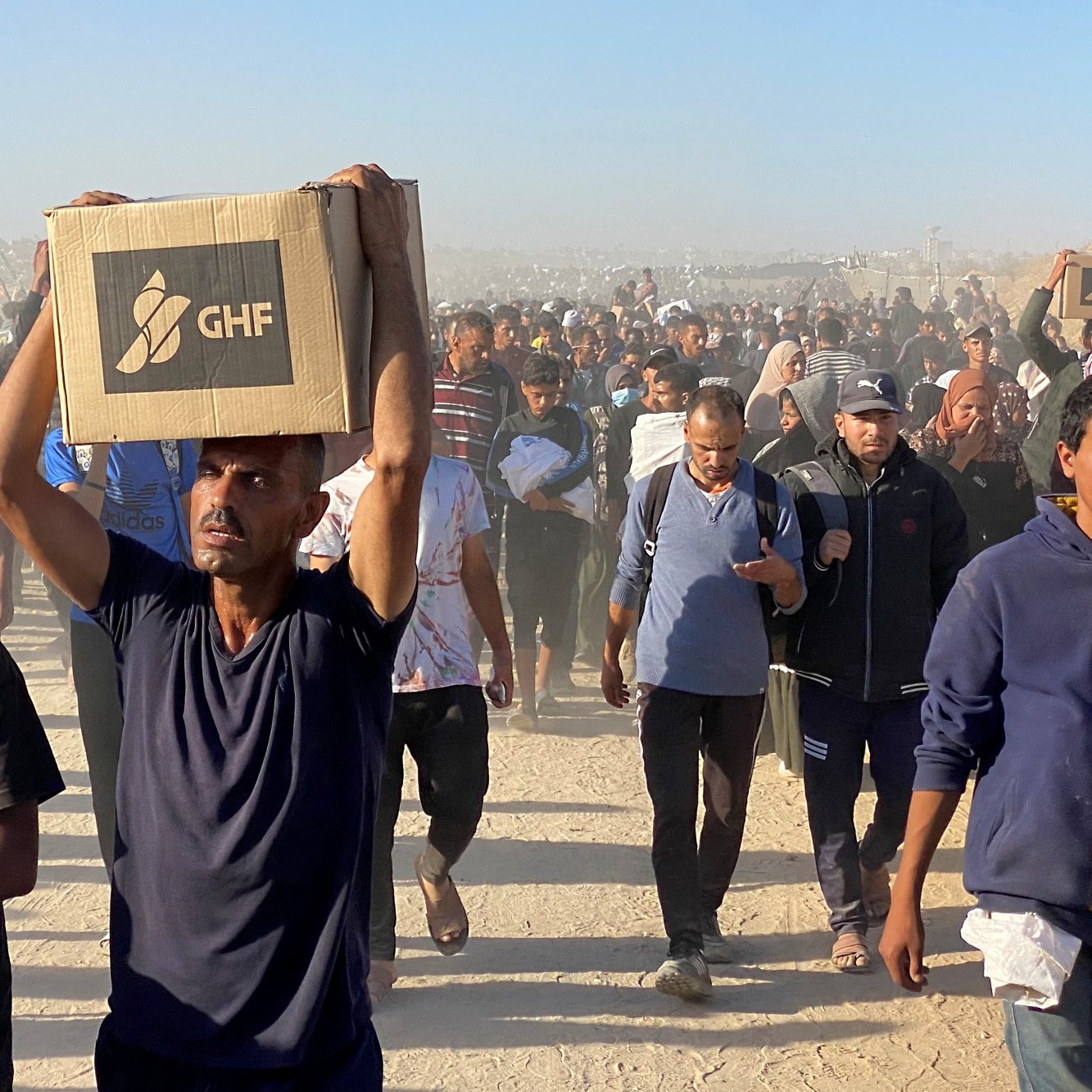 گروهی از مردان در حال حرکت در یک مکان گرد و غبارآلود، برخی بارهایی بر دوش دارند.