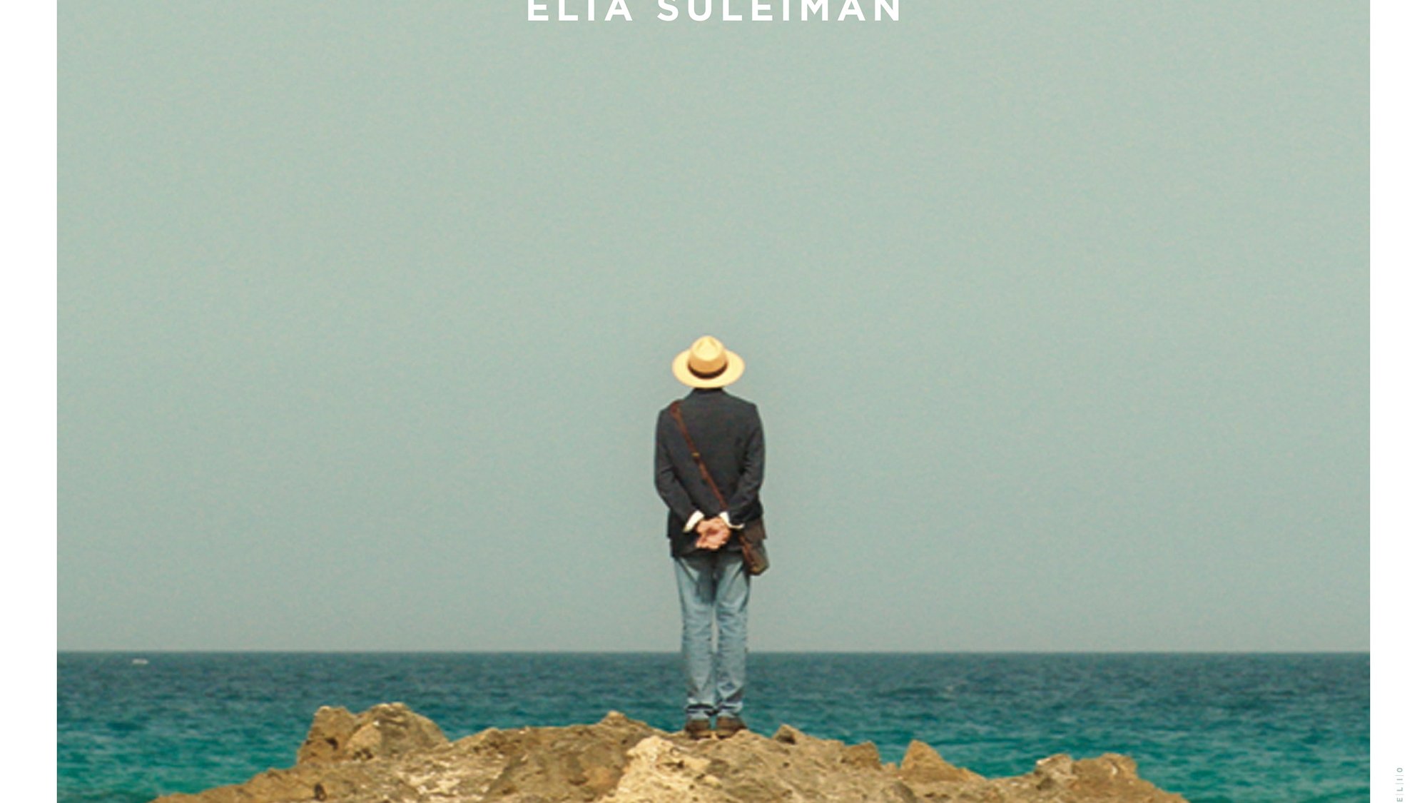 L'image représente une affiche de film intitulée "It Must Be Heaven", réalisé par Elia Suleiman. On y voit un homme de dos, portant un chapeau, se tenant debout sur un rocher au bord de la mer. L'horizon est dégagé, avec un ciel bleu clair. Le titre du film est inscrit en lettres blanches en bas de l'affiche, avec également le nom du réalisateur. L'ensemble de l'image évoque une ambiance contemplative et poétique.