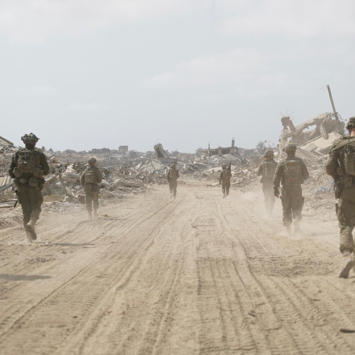 Des soldats marchent sur un chemin poussiéreux, entourés de débris et de ruines.