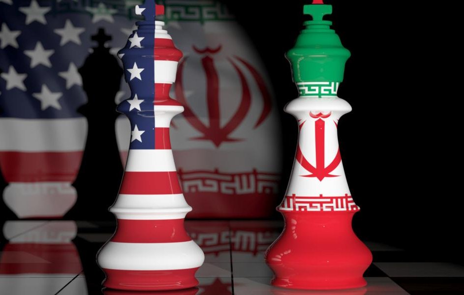 L'image représente des pièces d'échecs en forme de rois, une avec les couleurs du drapeau américain et l'autre avec celles du drapeau iranien. En arrière-plan, on peut voir des ombres ou des motifs représentant ces deux pays. La scène évoque une confrontation symbolique entre les États-Unis et l'Iran, souvent associée à des tensions géopolitiques. Le fond sombre renforce l'aspect dramatique de l'image.