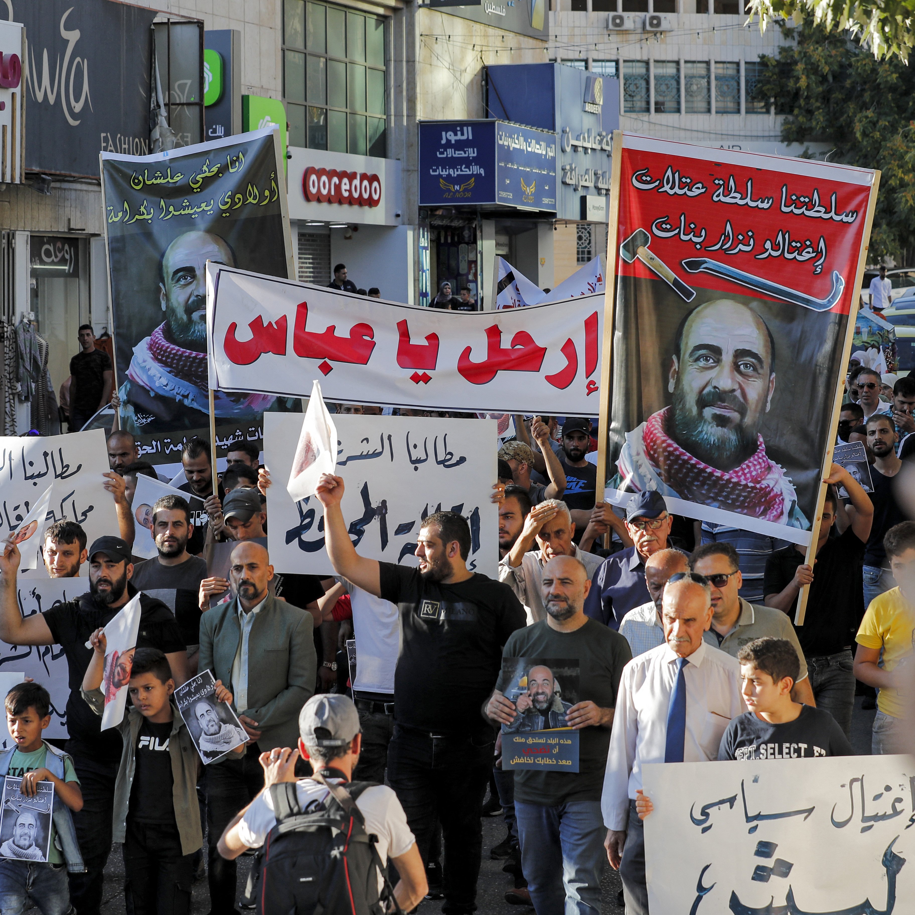 الصورة تُظهر مجموعة من المتظاهرين في شارع يجمعهم الاحتجاج، حيث يحملون لافتات كبيرة تحمل شعارات ومطالب تعبر عن قضايا معينة. يظهر في الصورة عدد من الرجال والنساء والأطفال، وبعضهم يرتدي القمصان بتصاميم مختلفة. يبدو الحشد نشطاً ومتفاعلاً، واللافتات مكتوبة باللغة العربية، مما يدل على أن التظاهر يتناول قضايا محلية. الجو يبدو حماسياً مع وجود بعض السيارات في الخلفية.