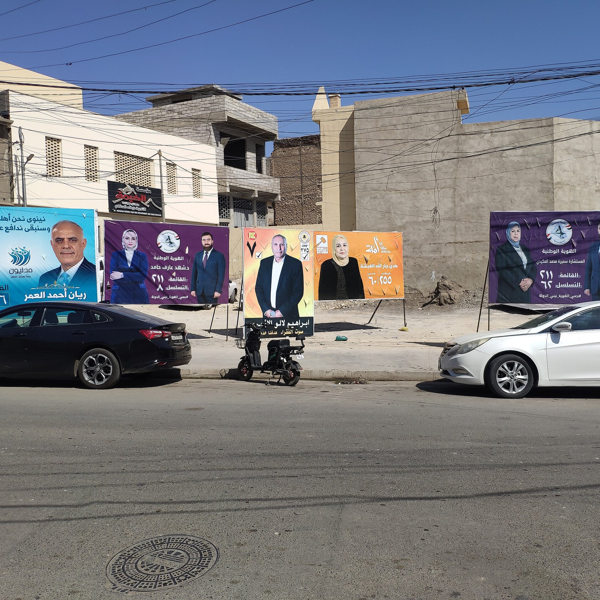 Una strada con diversi manifesti pubblicitari colorati su un muro di fondo.