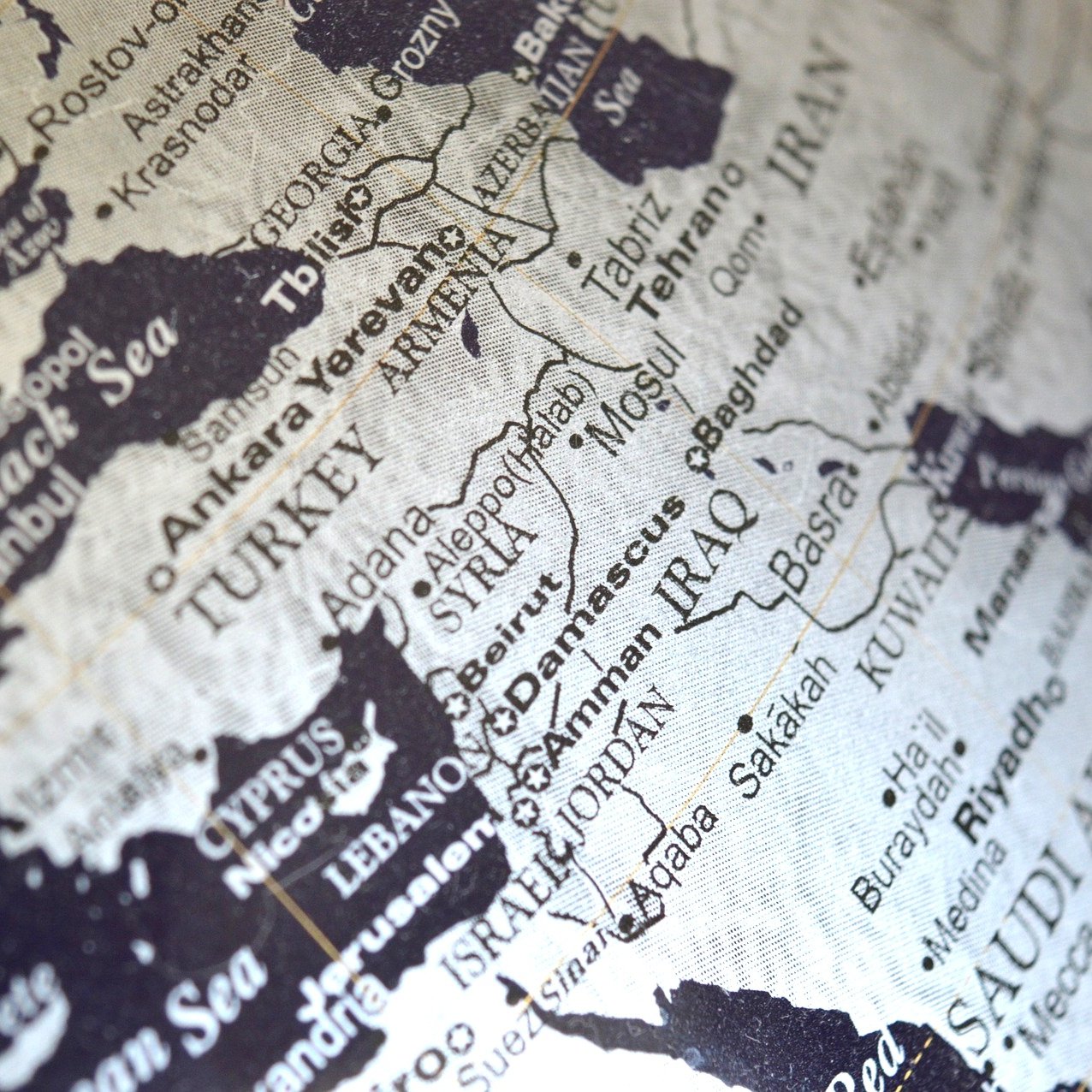 L'image montre une carte en noir et blanc d'une région qui inclut le Moyen-Orient et certaines parties de l'Europe et de l'Asie. On peut distinguer des pays comme la Turquie, l'Iran, l'Irak et l'Arabie Saoudite. Les noms des villes et des pays sont inscrits en lettres claires, créant un contraste avec le fond noir. La carte semble stylisée, donnant une impression de vintage ou d'art graphique.