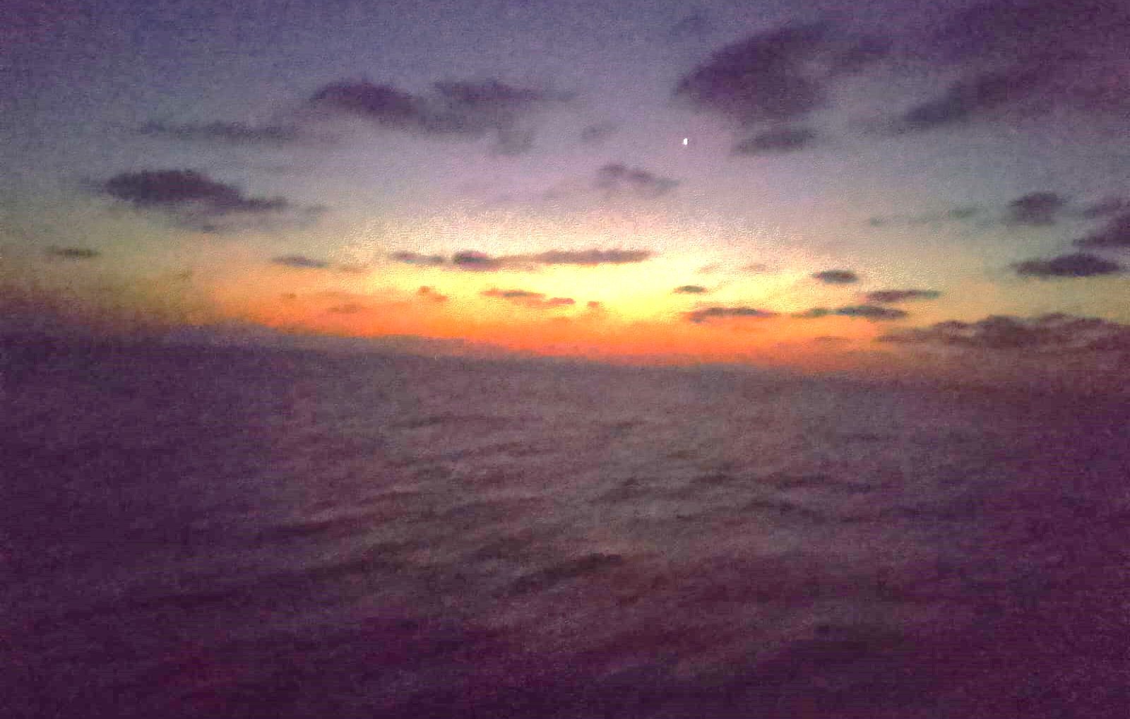 Un coucher de soleil aux couleurs chaudes se reflète sur la mer calme.