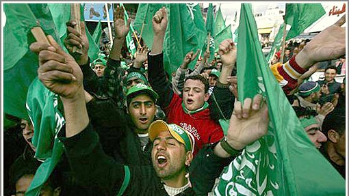 L'image montre une foule de personnes brandissant des drapeaux verts, manifestant de manière énergique. On peut voir des groupes de jeunes hommes exprimer leur enthousiasme, certains chantant ou criant. L'atmosphère semble festive, avec des expressions de joie et de solidarité parmi les participants. Les vêtements et accessoires des manifestants reflètent une allure colorée, souvent associée à des symboles politiques ou culturels.