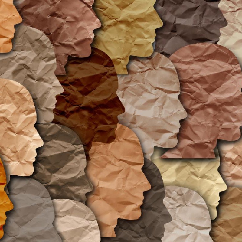 تظهر الصورة مجموعة من الوجوه البشرية المصنوعة من ورق ملتوي بألوان مختلفة تتراوح بين درجات البيج والبني. تعكس هذه الألوان تنوع البشرة، حيث يتم ترتيب الوجوه بشكل متداخل، مما يخلق تأثيرًا فنيًا مميزًا. تبرز الأشكال والظلال الملتوية، مما يعطي انطباعًا عن الحركة والتنوع الثقافي.