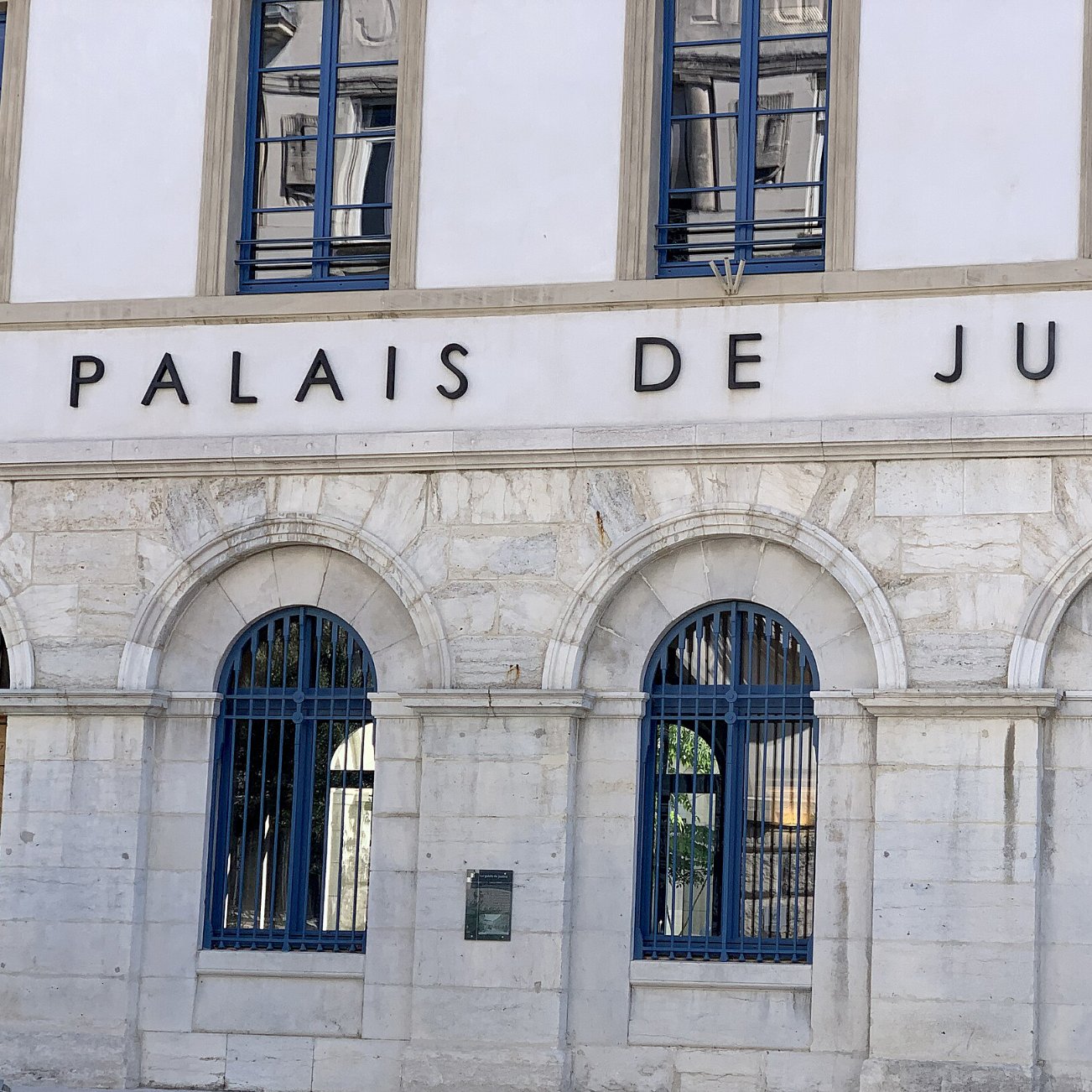 Façade d'un bâtiment imposant avec l'inscription "Palais de Justice" et des fenêtres à arcs.