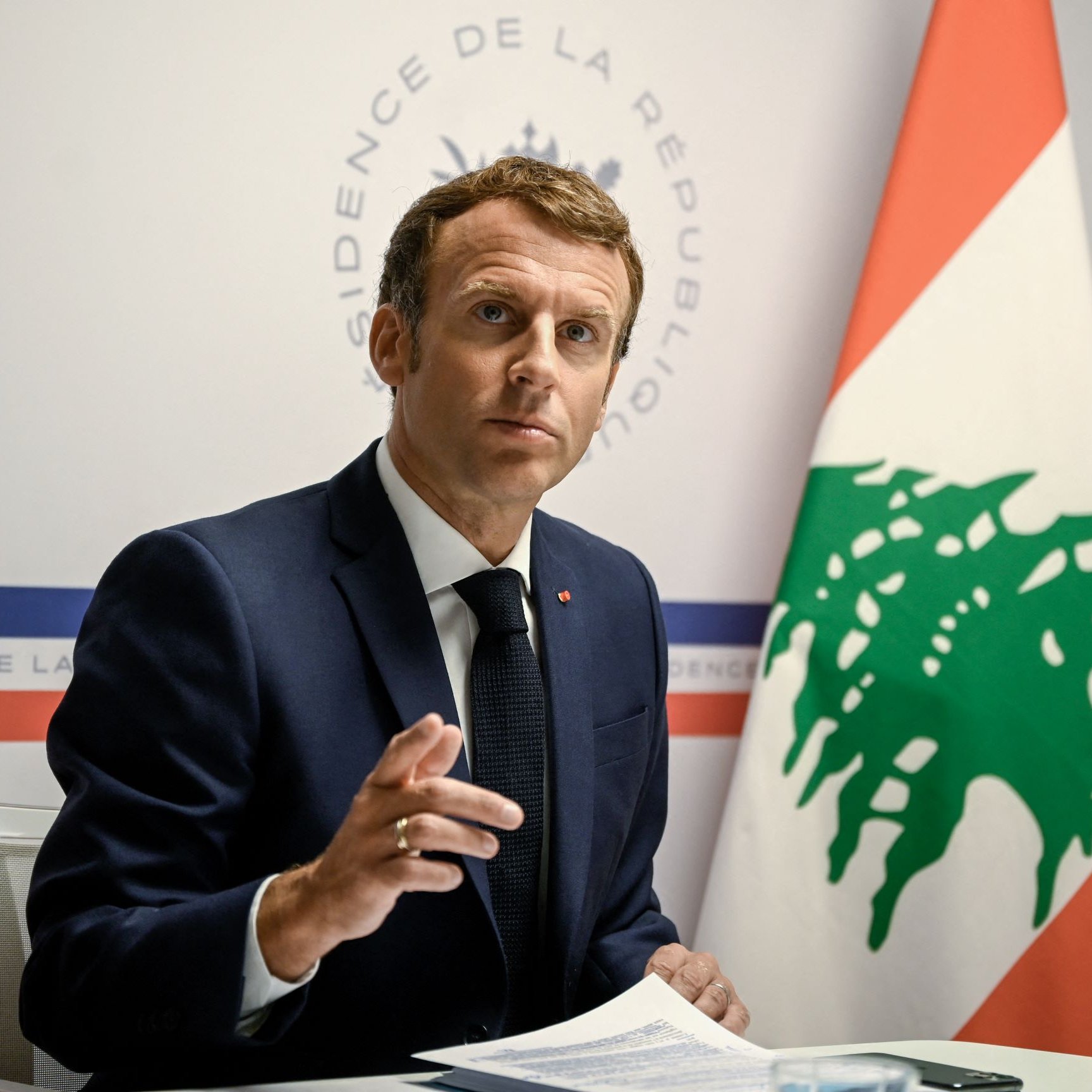 L'image montre un homme en costume, assis à une table, s'adressant à un public. Il semble être en train de faire un discours ou de répondre à des questions, avec une expression sérieuse. En arrière-plan, on peut voir un drapeau libanais ainsi qu'un logo indiquant "Présidence de la République". L'ambiance de l'image évoque un contexte officiel et diplomatique.