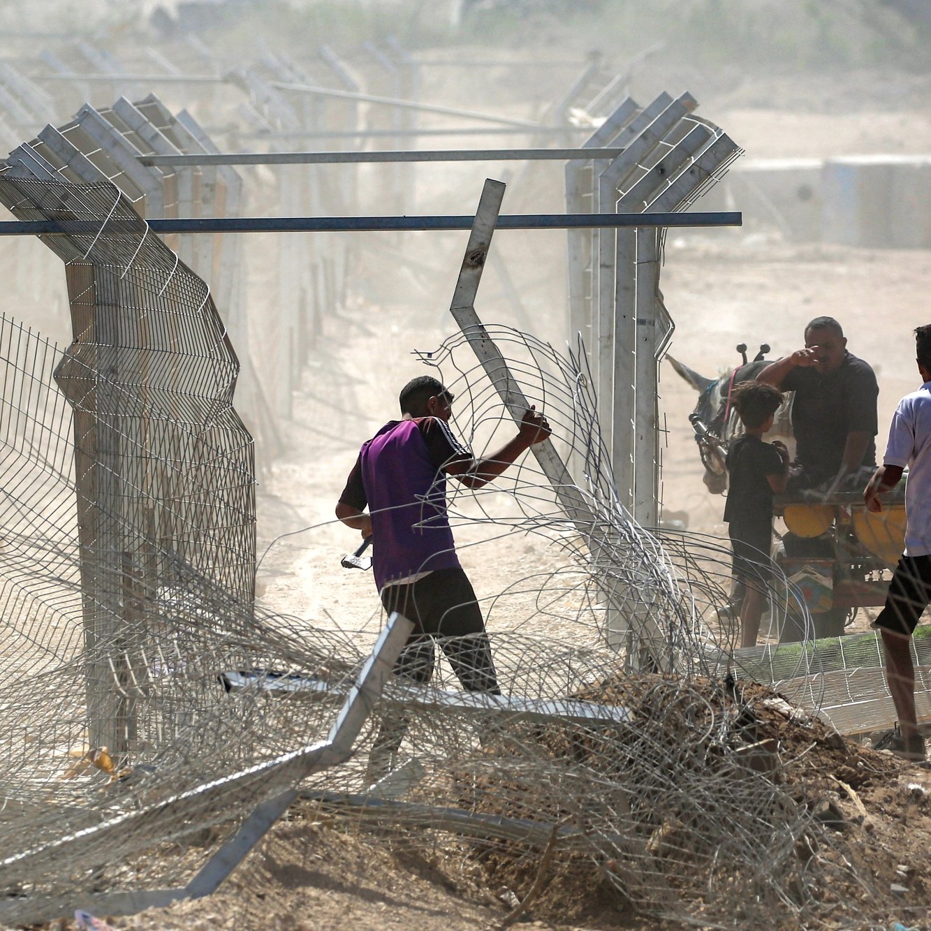 Des hommes manipulent des barbelés près d'une clôture dans un environnement poussiéreux.