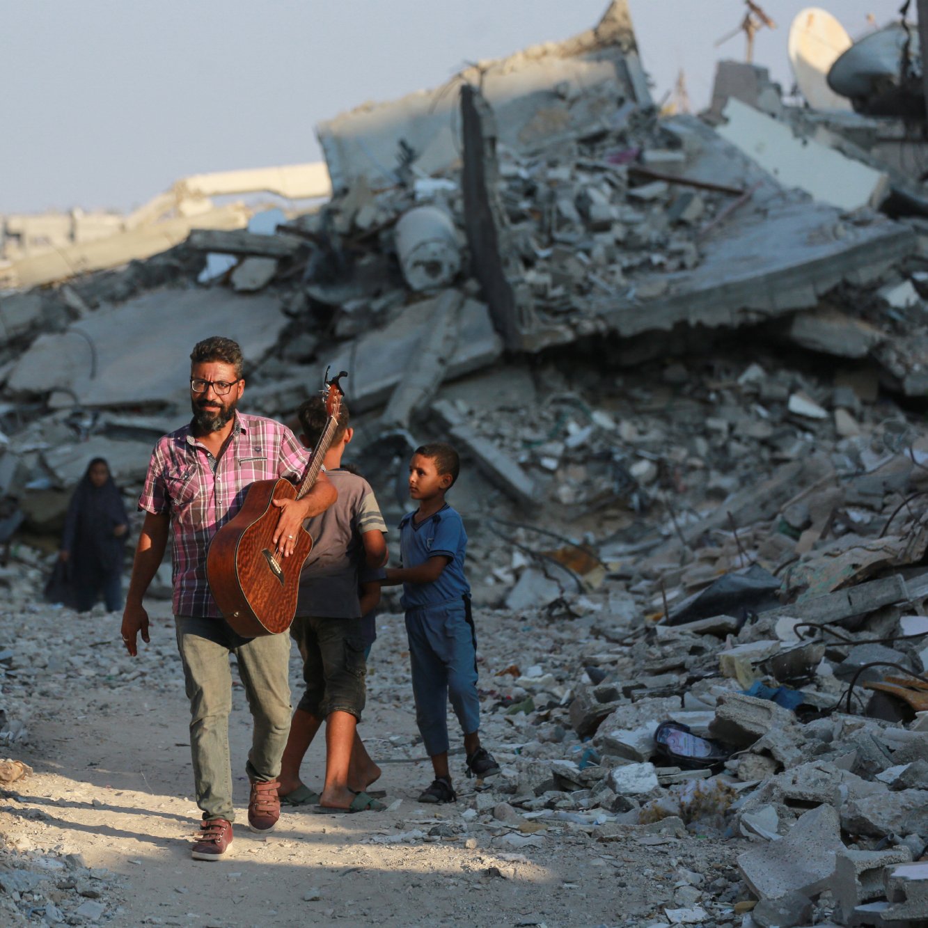 تصویر یک مرد را نمایش می‌دهد که در حال حرکت در میان ویرانه‌های یک منطقه تخریب‌شده است. او یک گیتار به دوش دارد و به نظر می‌رسد در حال نواختن یا آماده نواختن موسیقی باشد. دو کودک نیز به او نزدیک هستند، یکی از آنها به مرد وابسته است و به نظر می‌رسد او را دنبال می‌کند. در پس‌زمینه، آوار و خرابه‌های ساختمان‌ها دیده می‌شود که نشانه‌ای از یک بحران یا جنگ را نشان می‌دهد. نورخورشید در آسمان دیده می‌شود که ممکن است تصاویری از امید را القا کند.