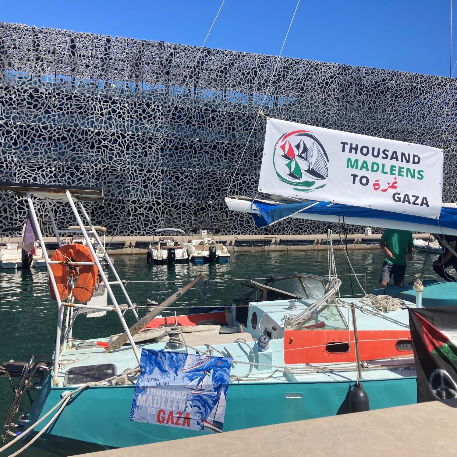 Una barca in un porto con un banner che supporta Gaza e un fondale moderno.