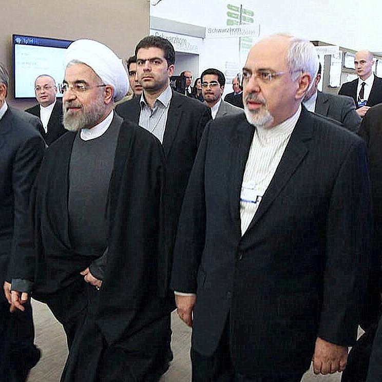 این تصویر گروهی از افراد را نشان می‌دهد که در حال حرکت به سمت یک مکان هستند. یکی از آنها به وضوح لباس روحانیت پوشیده و دیگران نیز به طور رسمی لباس پوشیده‌اند. به نظر می‌رسد این افراد در یک رویداد یا کنفرانس رسمی شرکت کرده‌اند. محیط تصویر ممکن است یک مکان اداری یا کنفرانس باشد که نشان‌دهنده تعاملات سیاسی یا اقتصادی است.