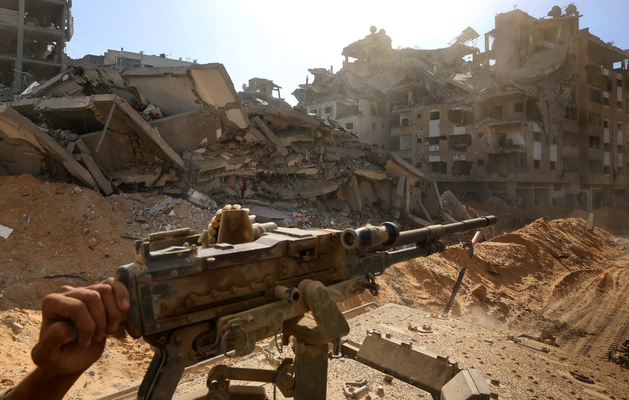 Un fusil pointé vers des bâtiments en ruines, sous un ciel lumineux.