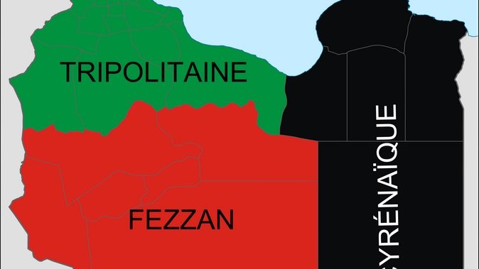 L'image montre une carte de la Libye, divisée en trois régions principales. La partie supérieure est la Cyrénaïque, représentée en noir. La région au centre est le Fezzan, en rouge, tandis que la partie supérieure gauche est la Tripolitaine, indiquée en vert. Chaque couleur représente une région distincte du pays.