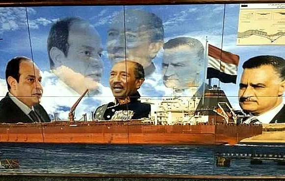 L'image présente une fresque murale qui montre un grand cargo au premier plan, naviguant sur l'eau. En arrière-plan, plusieurs portraits en superposition de différentes figures politiques égyptiennes, évoquant probablement des présidents ou dirigeants historiques. L'ensemble crée une composition qui semble célébrer l'histoire maritime et politique de l'Égypte, en particulier autour du canal de Suez. Des éléments graphiques comme le logo du canal et une carte en haut à droite ajoutent au contexte maritime.