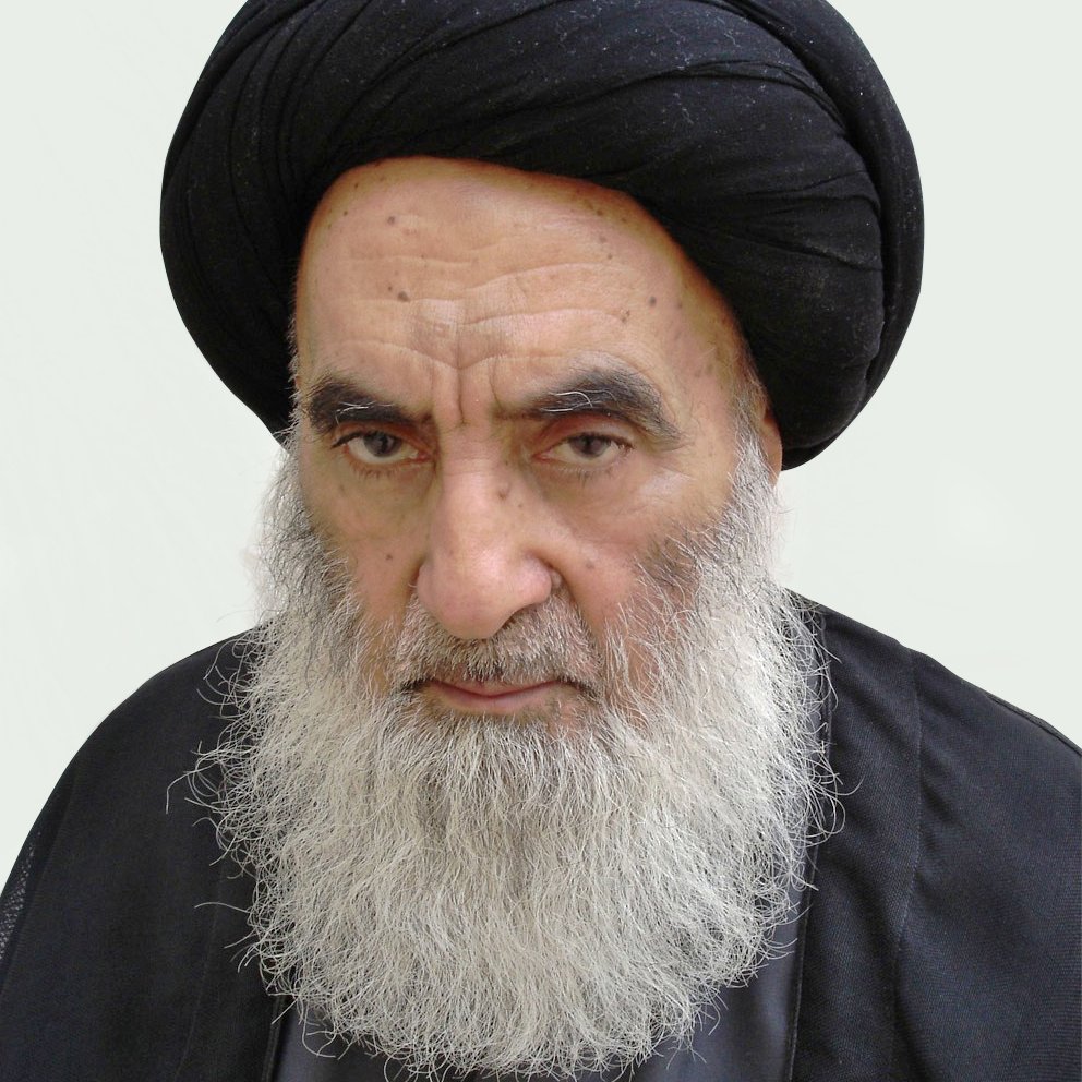 الصورة تُظهر رجلًا مسنًّا ذو لحية بيضاء وشعر داكن تحت عمامة سوداء. يبدو عليه الوقار والجدية. يرتدي ثوبًا داكنًا، مما يعكس نمطًا تقليديًا في اللباس. الخلفية بسيطة ووردية اللون، مما يبرز ملامح وجهه.