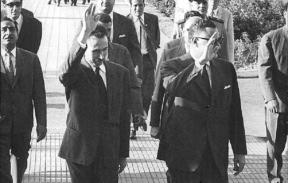 تظهر الصورة مجموعة من الرجال يسيرون على ممر، بعضهم يلوح بيديه. يبدو أن الصورة مأخوذة في فترة تاريخية معينة حيث يرتدي معظمهم بدلات رسمية. كما يظهر في الخلفية بعض الأشخاص الذين يسيرون بطريقة منظمة، بالإضافة إلى تشكيلات من الأشخاص في الجانب. تعكس الصورة أجواء رسمية أو حدثاً مهماً.