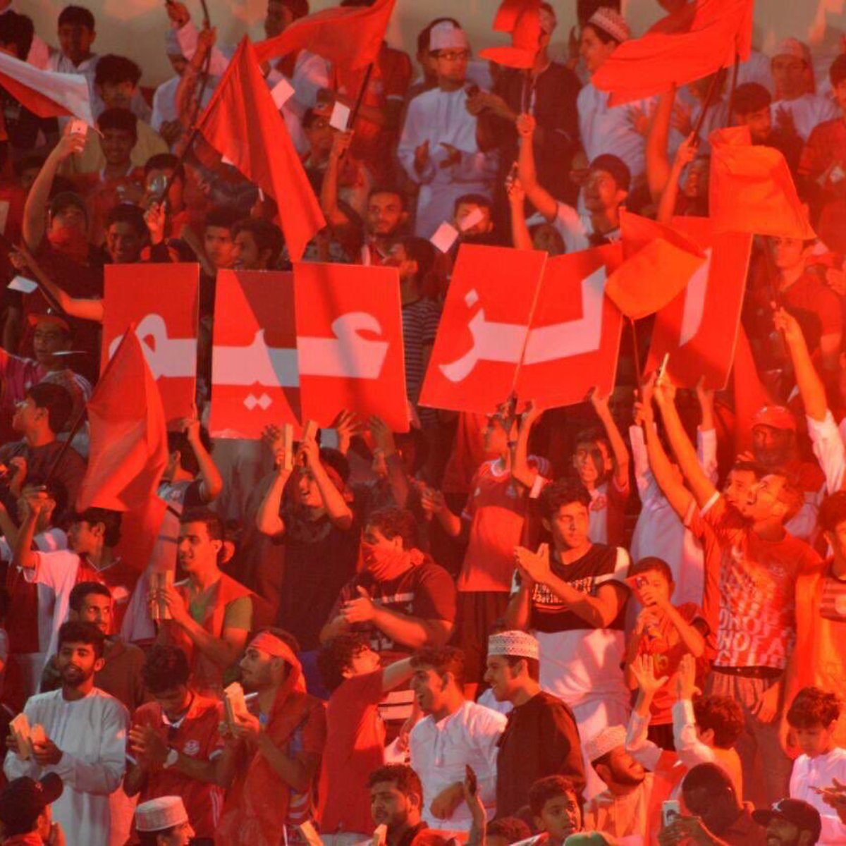 Supporters en fête, agitant des drapeaux rouges et des affichettes dans une ambiance dynamique.