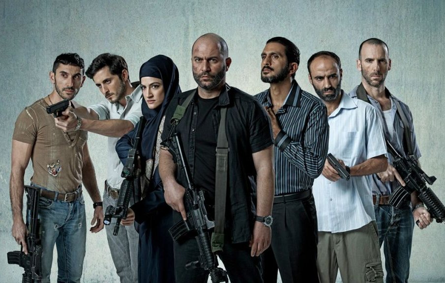 L'image montre un groupe de sept personnes armées, se tenant debout sur un fond gris. Ils ont des expressions déterminées et semblent en position de confrontation. Certains d'entre eux tiennent des armes à feu, tandis qu'une femme porte un hijab et se tient au milieu du groupe. Les hommes sont vêtus de vêtements variés, allant de casual à militaire. L'atmosphère est intense et pourrait suggérer un contexte d'action ou de tension.