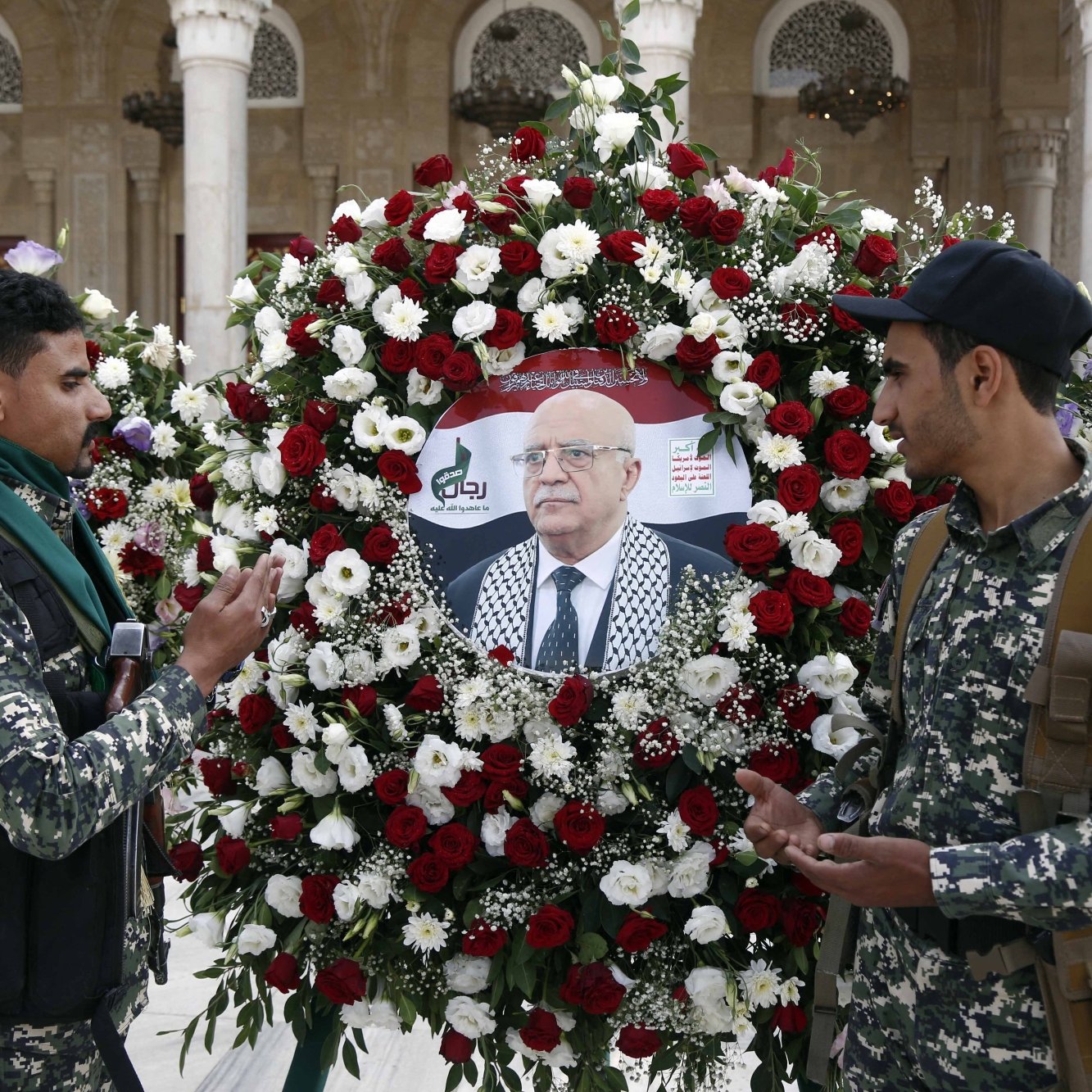 صورة لجنود يقفون أمام إكليل زهور يحمل صورة شخصية مهمة.