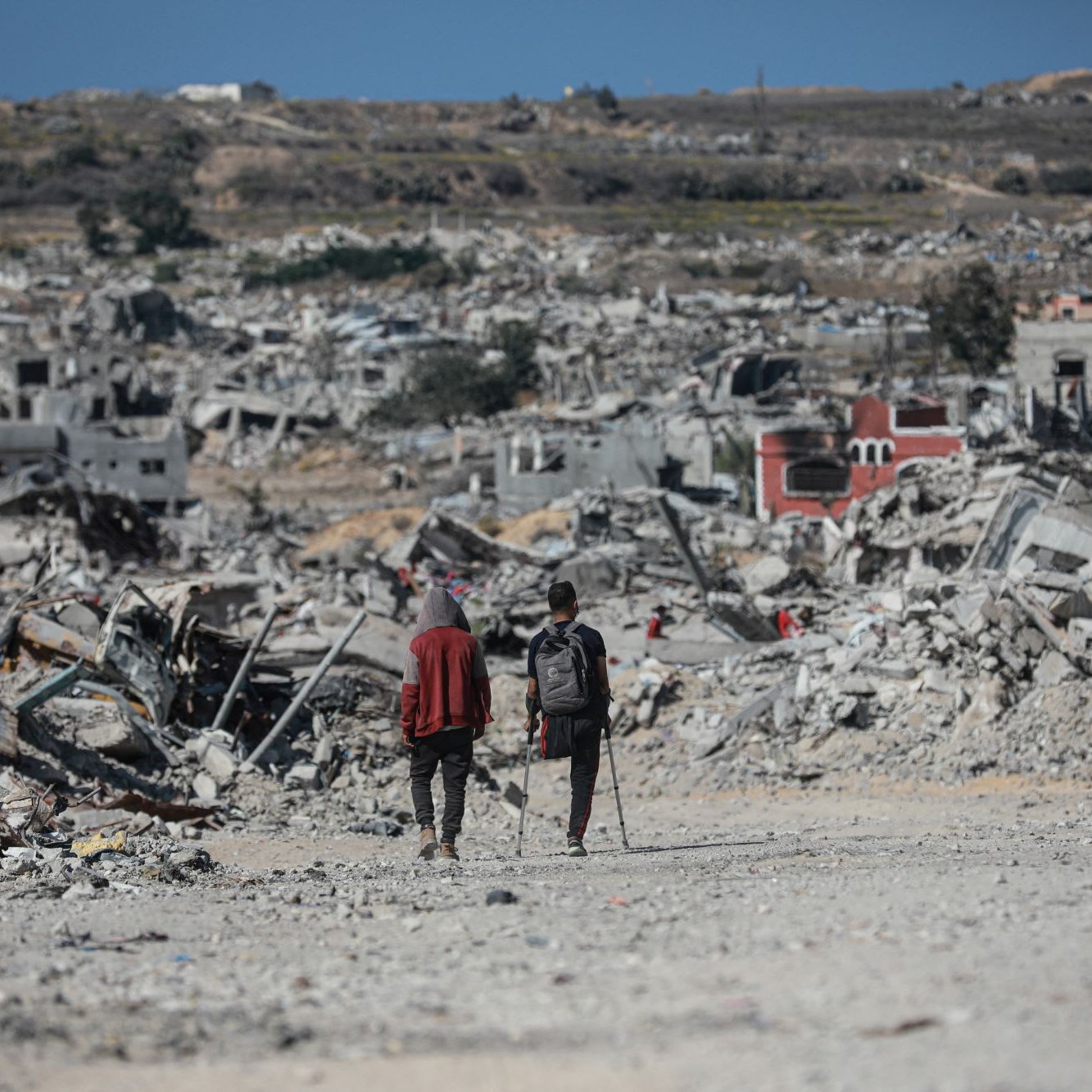 Deux personnes marchent dans un paysage de destruction, entourées de débris.