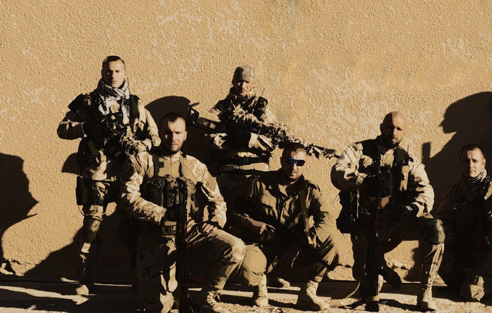 L'image montre un groupe de soldats en tenue militaire. Ils sont positionnés à la fois debout et accroupis, avec des armes à feu en main. L'arrière-plan est une surface murale de couleur beige, ce qui suggère un environnement désertique. Les soldats portent des uniformes camouflés et semblent prêts pour une mission. L'éclairage est plutôt clair, mettant en valeur leurs expressions et leurs équipements.