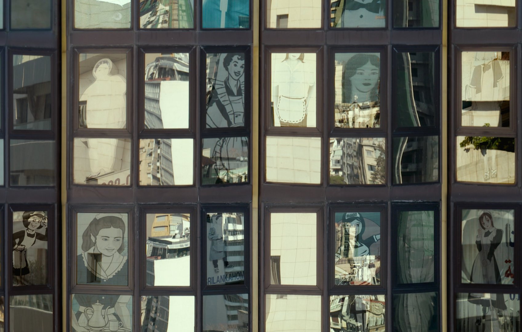 L'image montre une façade de bâtiment avec de grandes fenêtres. À travers ces fenêtres, on peut voir des reflets de la ville environnante ainsi que des illustrations ou des portraits de personnes qui semblent être intégrés dans les carreaux. Les illustrations sont stylisées et en noir et blanc, ajoutant un contraste intéressant avec les reflets colorés des bâtiments environnants. Cette composition crée une atmosphère visuelle dynamique et intrigante.