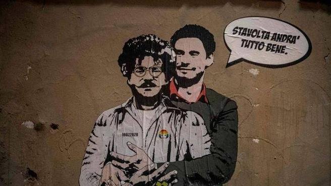 L'immagine mostra un murale che ritrae due figure. Una di esse ha un aspetto distintivo, con occhiali e baffi, mentre l'altra indossa un completo elegante. Sullo sfondo, si può notare un muro di colore neutro, e sopra le figure è presente un testo in italiano che dice "Stai tranquillo, andrà tutto bene". Inoltre, nella parte inferiore della figura è scritta la parola "حرية" (che significa "libertà" in arabo). L'opera sembra trasmettere un messaggio di speranza e solidarietà.