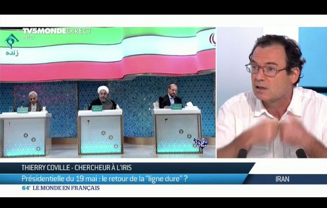 L'image présente une scène de débat ou de discussion, probablement liée à la politique. Au centre de l'image, on voit Thierry Coville, chercheur à l'IRIS, qui s'exprime avec des gestes. Derrière lui, trois personnes sont assises, dont l'une porte un costume clair. Le contexte semble lié à une élection présidentielle, évoquant des thèmes tels que la "ligne dure". L'image reflète un moment d'échange d'idées sur des enjeux politiques.