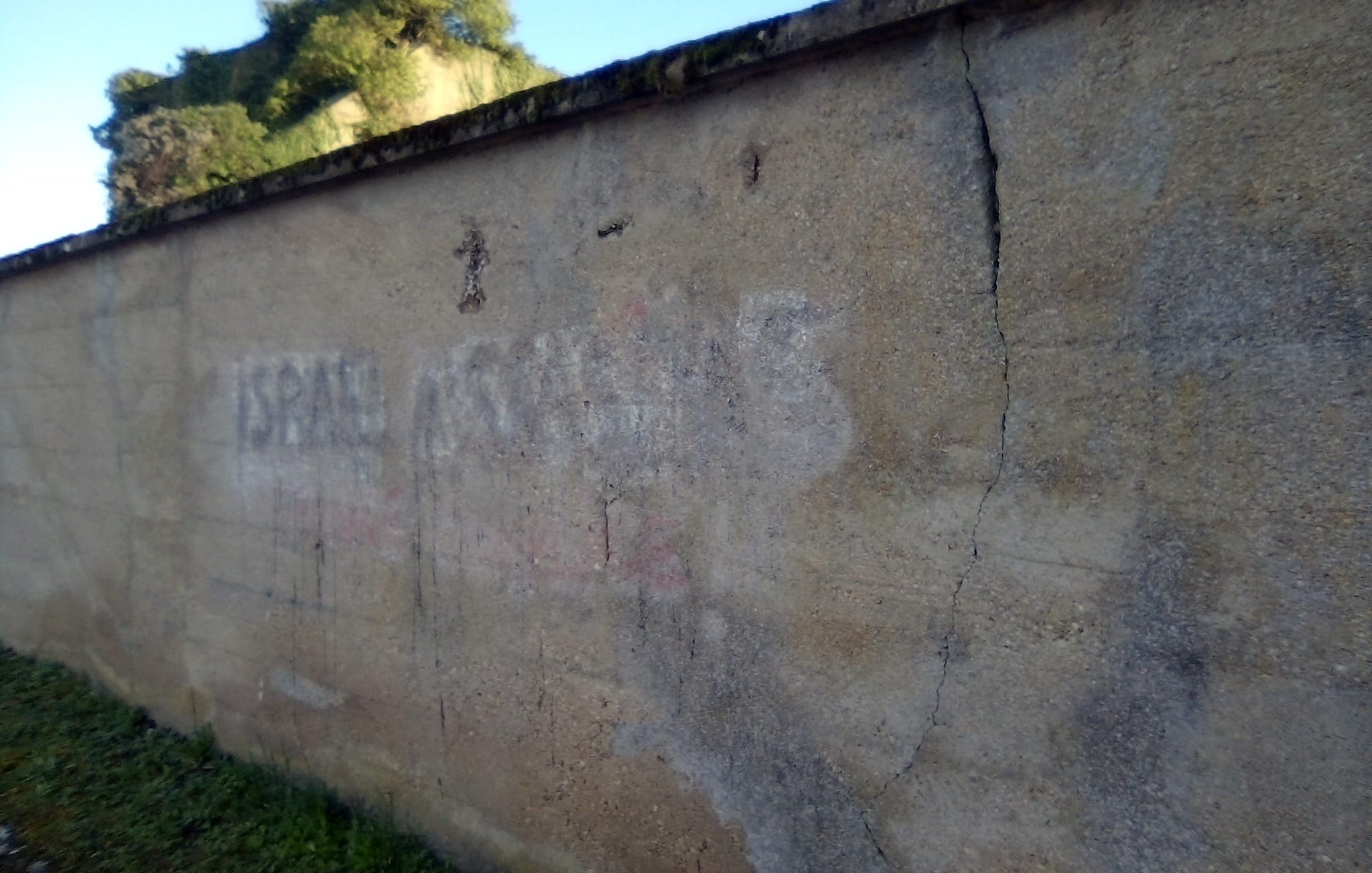 Mur en béton avec des inscriptions effacées et des fissures, sous un ciel bleu.