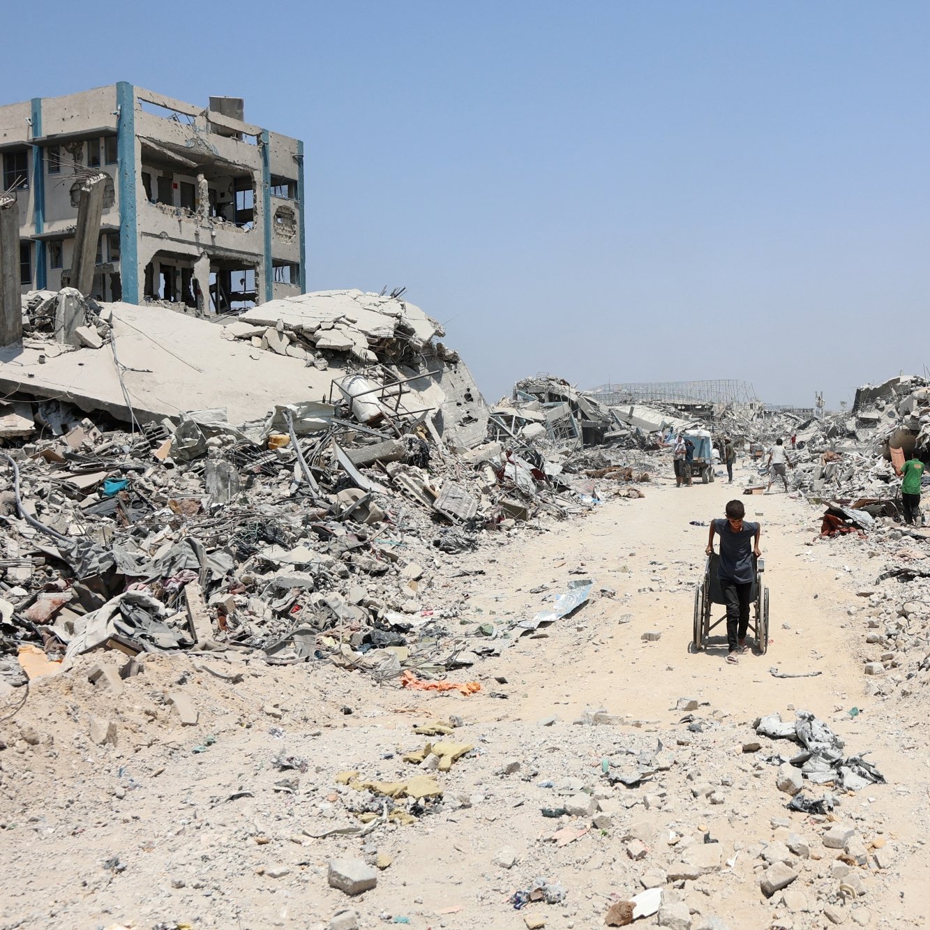 A person in a wheelchair navigates a debris-filled street amid collapsed buildings.